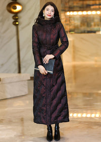 Model holding a black clutch purse wearing a deep wine shimmering belted maxi down parka coat