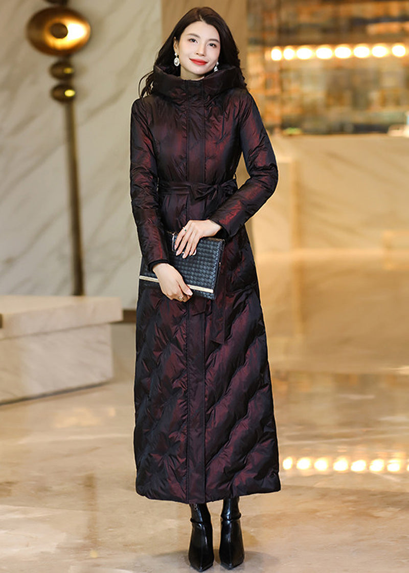 Model holding a black clutch purse wearing a deep wine shimmering belted maxi down parka coat