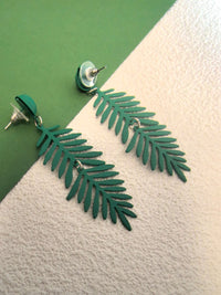 Close-up of two matte forest-green fern-leaf dangle earrings, showing the post and clutch backings, set against a background split between dark green and textured white.