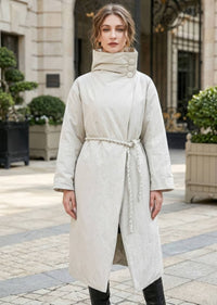 Front view of woman wearing beige high neck asymmetric down coat with button details and rope waist tie