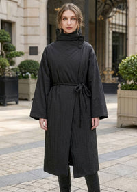 Front view of woman wearing black asymmetric high neck longline down coat with black braided rope belt