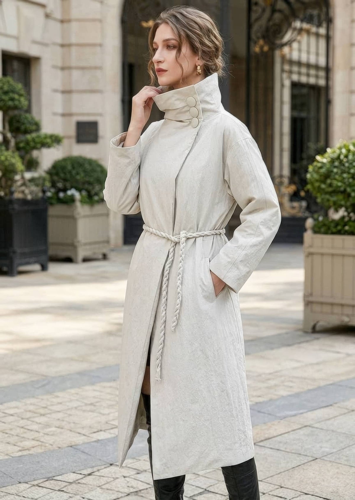 Three-quarter shot of woman wearing beige asymmetric high collar down coat with braided rope waist tie