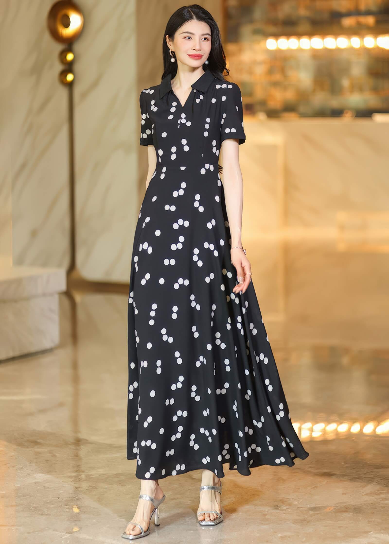 Rear view of a woman wearing a black and white polka dot maxi dress, showing the flowing skirt and long, dark wavy hair.