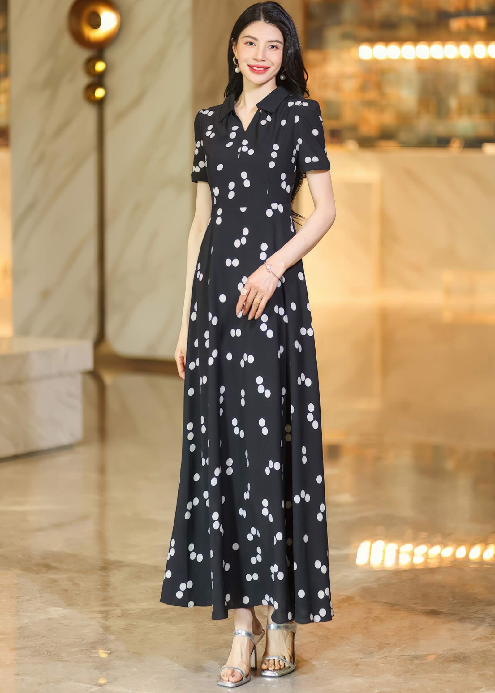 "Portrait of a woman wearing a black lapel collar maxi dress with white polka dots, posing in a well-lit indoor lobby.