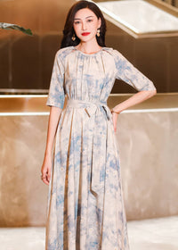 Mid-shot focusing on the upper body of a woman with her hand on her hip, wearing a gathered-neck cream maxi dress with an abstract blue floral watercolor print.