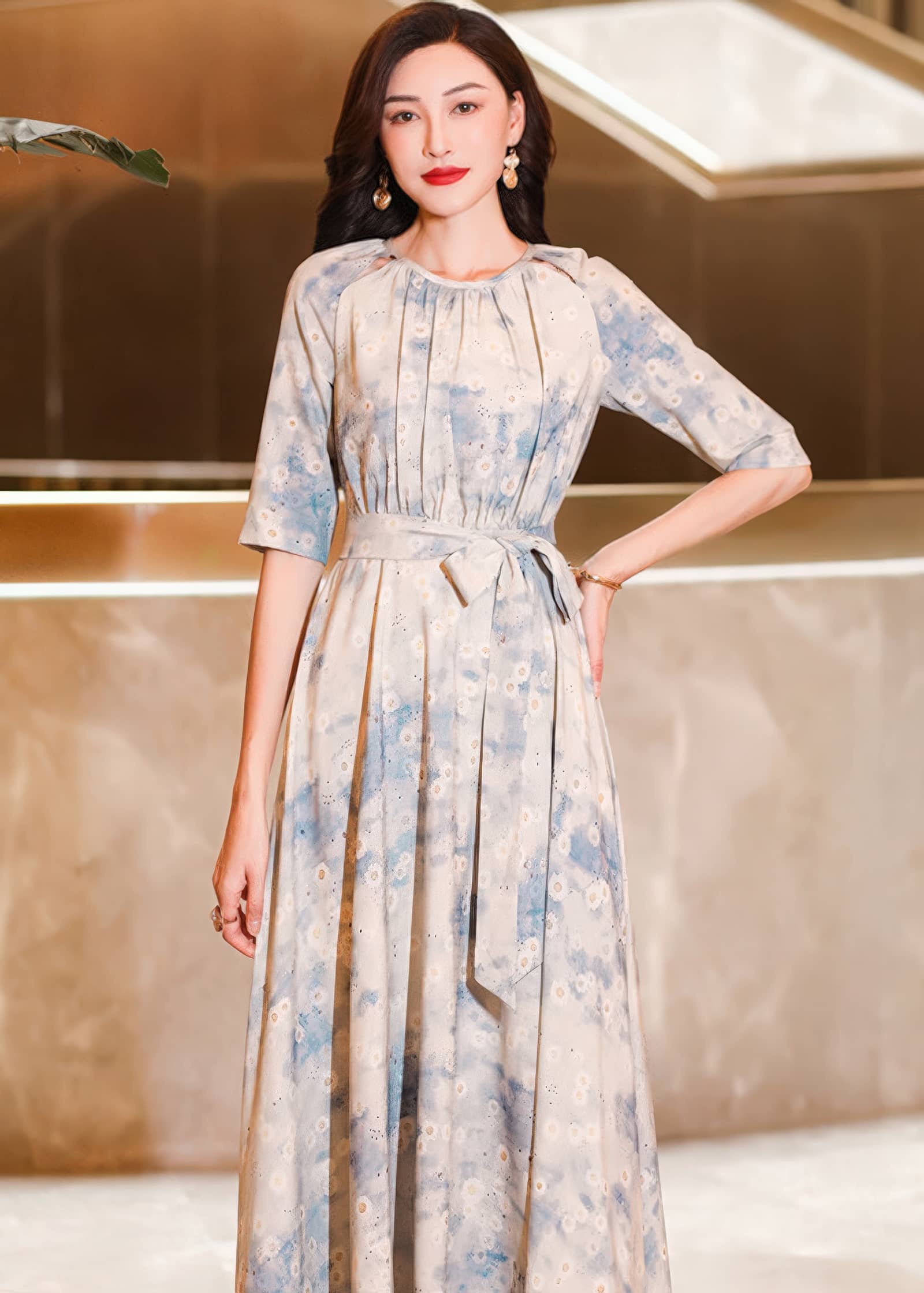Mid-shot focusing on the upper body of a woman with her hand on her hip, wearing a gathered-neck cream maxi dress with an abstract blue floral watercolor print.