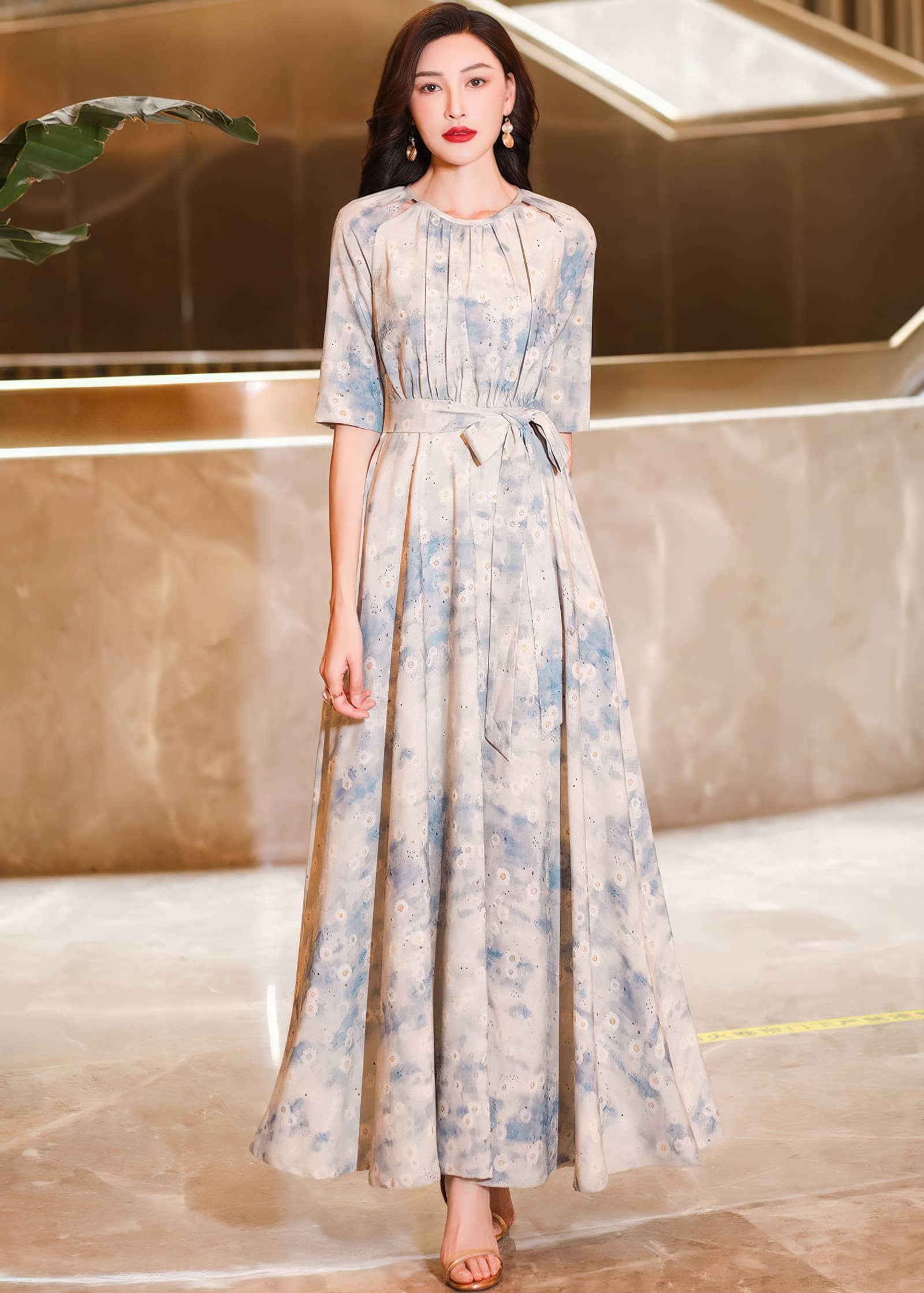 Full-length front portrait of a woman standing straight in a light cream and blue watercolor floral maxi dress with short sleeves and a flared skirt.