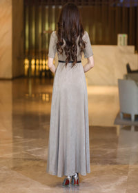 Back view of a woman with long wavy brown hair wearing a champagne A-line maxi dress with a thin black belt.