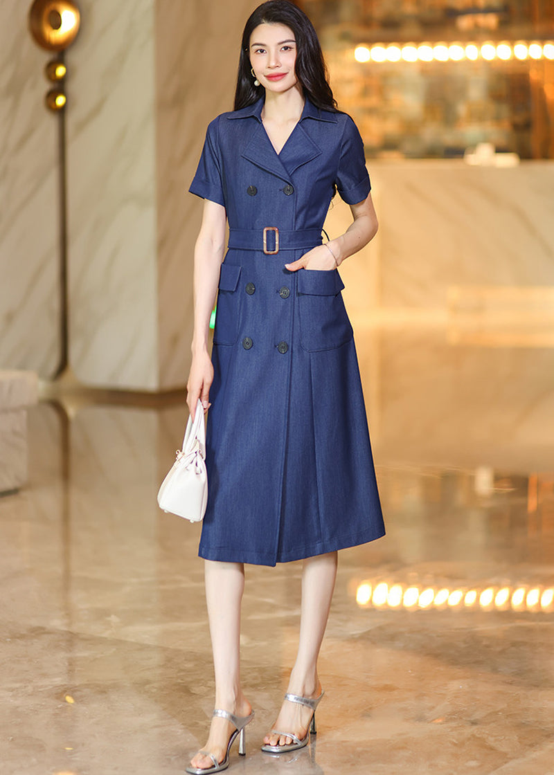 A stylish shot of a woman with one hand in the pocket of her double-breasted denim dress, holding a white purse in the other.