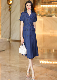 A full-length standing pose of a woman in a belted denim midi dress and silver heels, carrying a white leather tote bag.