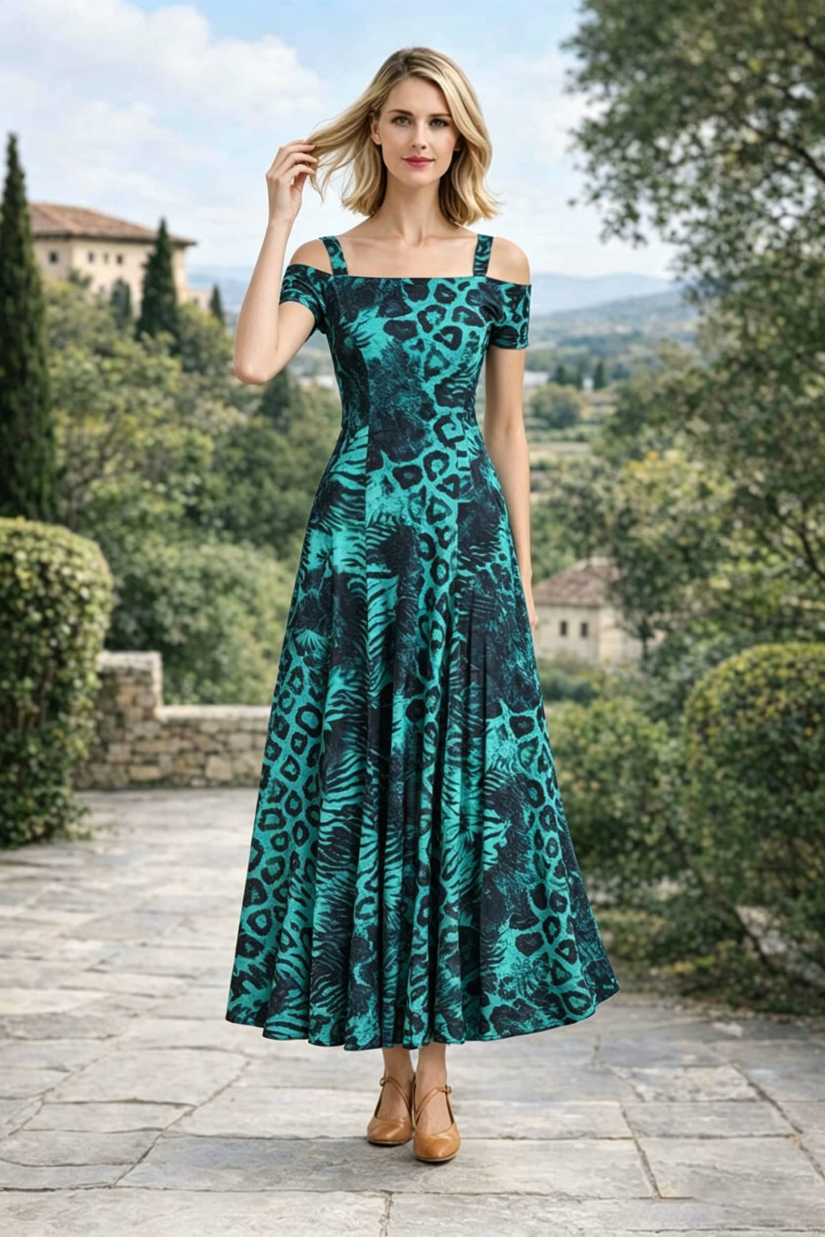 Front view of a woman with one hand in her hair, modeling an emerald green and black leopard print off-the-shoulder A-line maxi dress with thick straps, standing on an outdoor stone patio.