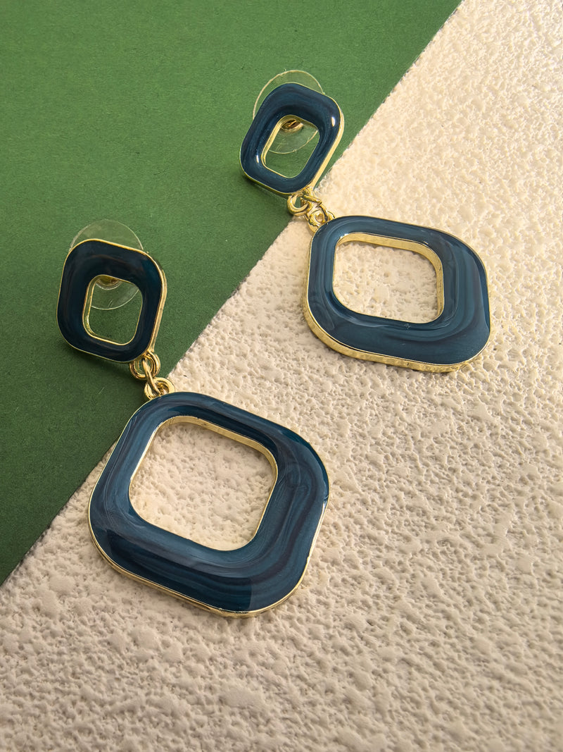 A close-up, eye-level shot of the blue enamel earrings against a two-toned background. The earrings have a shiny finish and a gold-tone base.