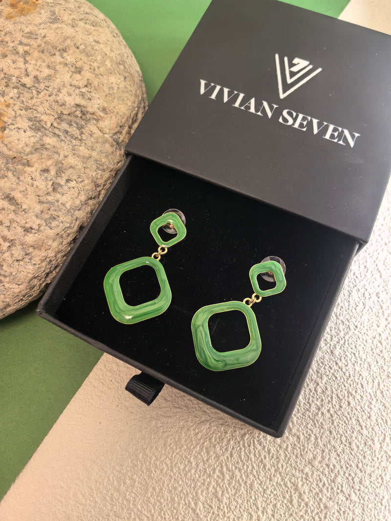 A pair of green enamel earrings displayed in their black box with the "VIVIAN SEVEN" logo. The earrings have a gold-tone base and a shiny finish.