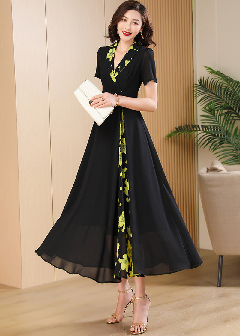  With Accessories,"A woman modeling a black V-neck maxi dress with green floral patterns, styled with a white clutch bag.