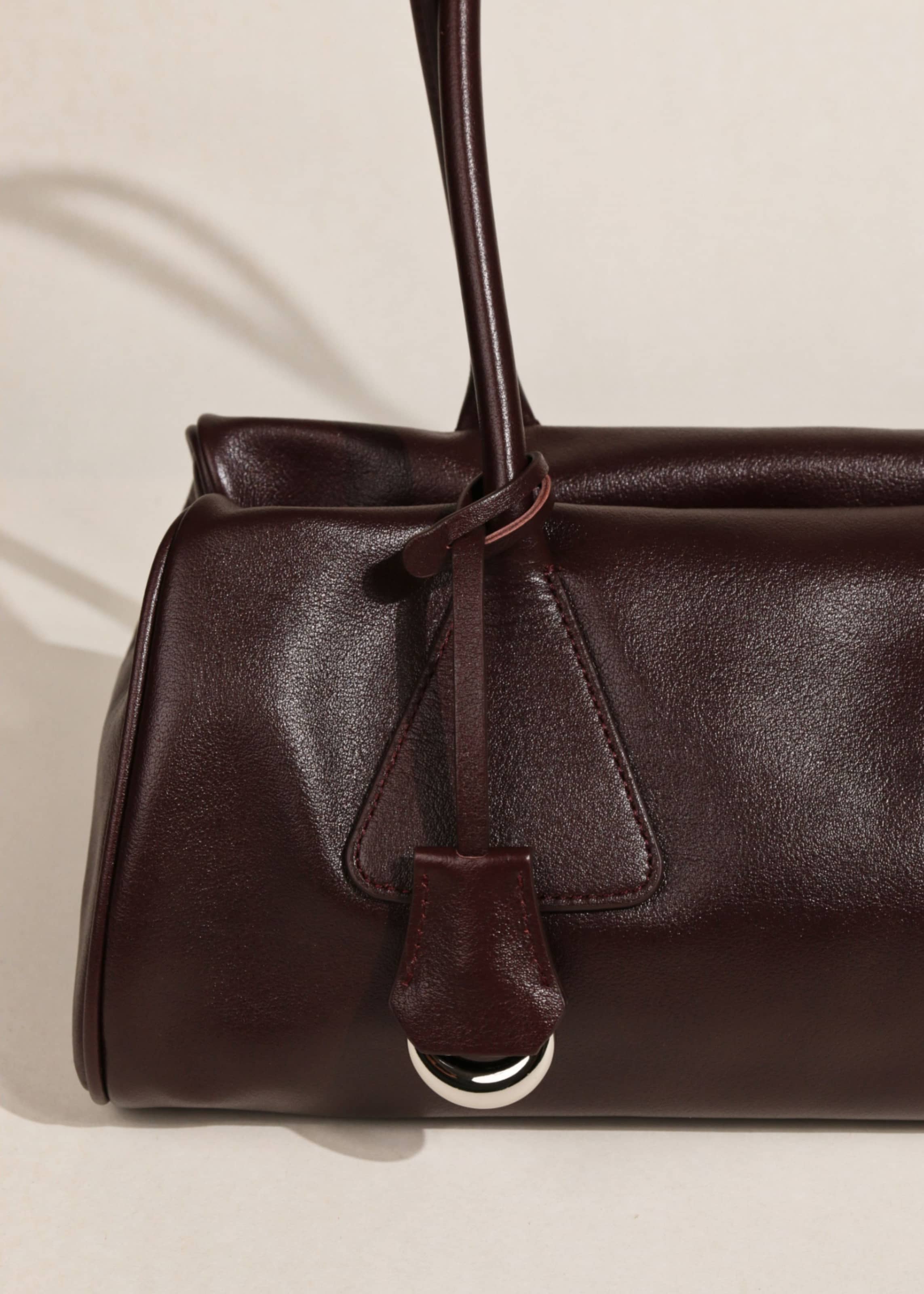 Close-up detail of smooth burgundy leather handbag texture with key fob and silver D-ring charm