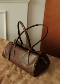 Three-quarter angle view of a brown leather baguette shoulder bag sitting on a neutral surface
