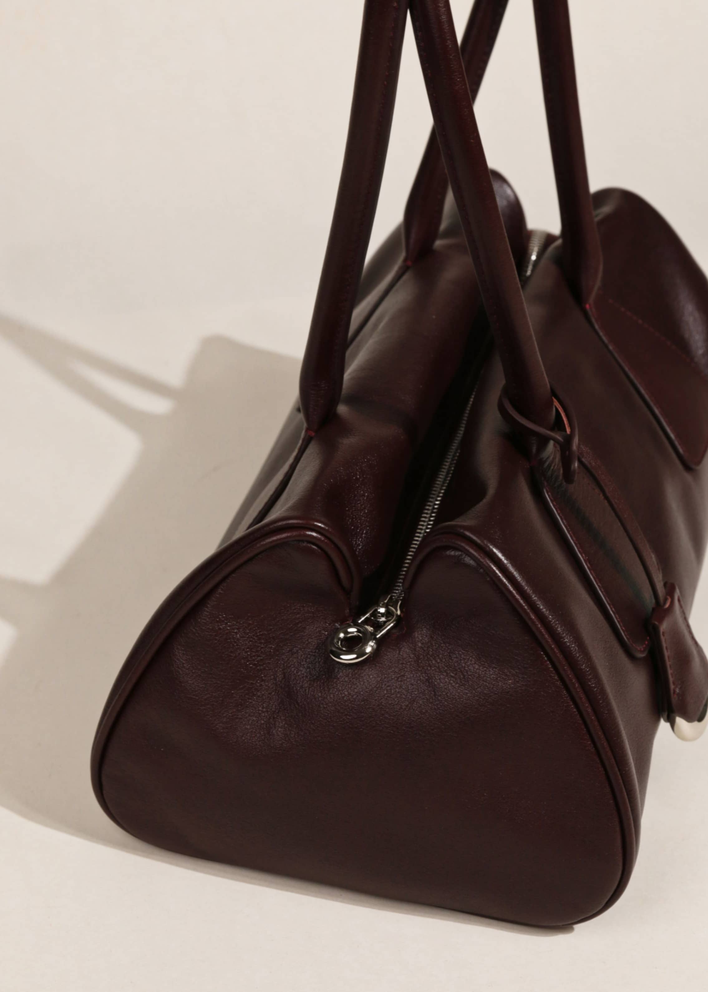 Close-up side view of a burgundy leather purse highlighting smooth metal zipper and rounded side profile