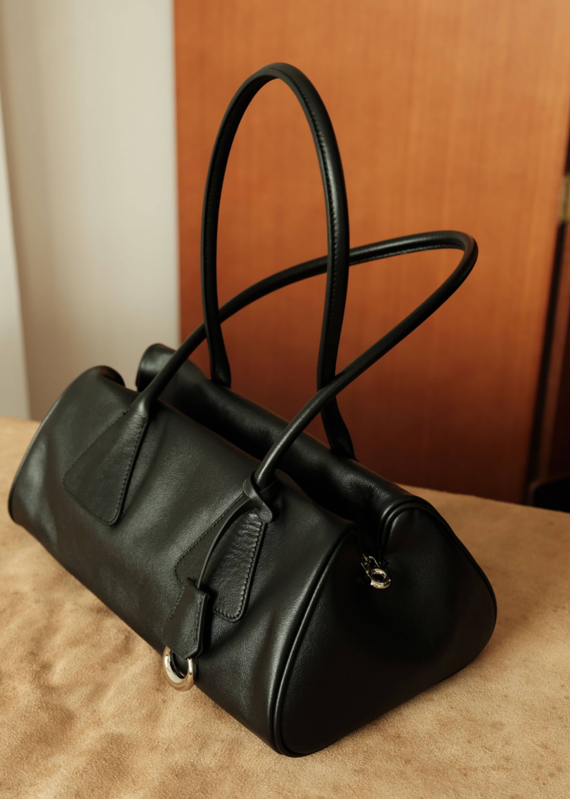 Side profile of a black genuine leather tote handbag showing smooth texture and spacious structure