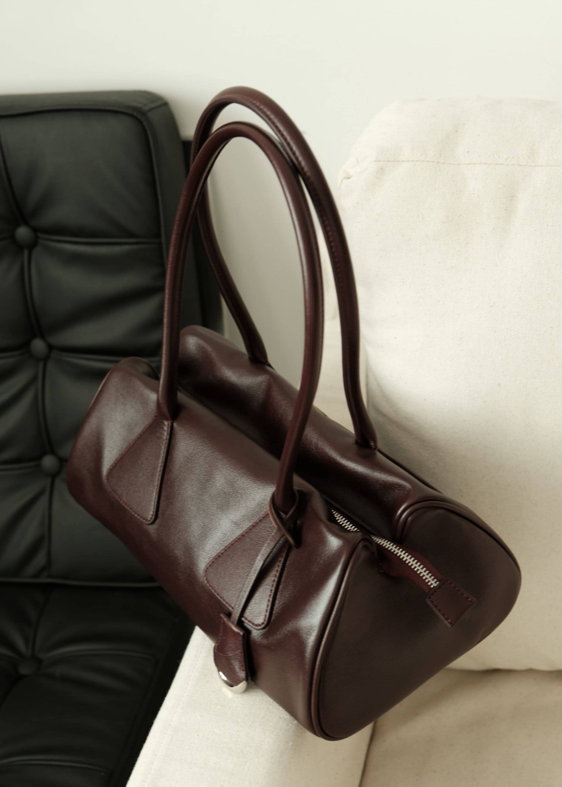 Deep burgundy leather shoulder handbag resting on a modern beige armchair