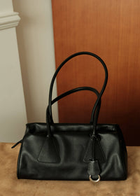 Front view of a classic black genuine leather shoulder handbag with long handles and key tag detail