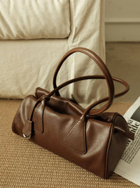 Top-side angle of a soft brown leather shoulder bag showcasing stitched triangle strap base details