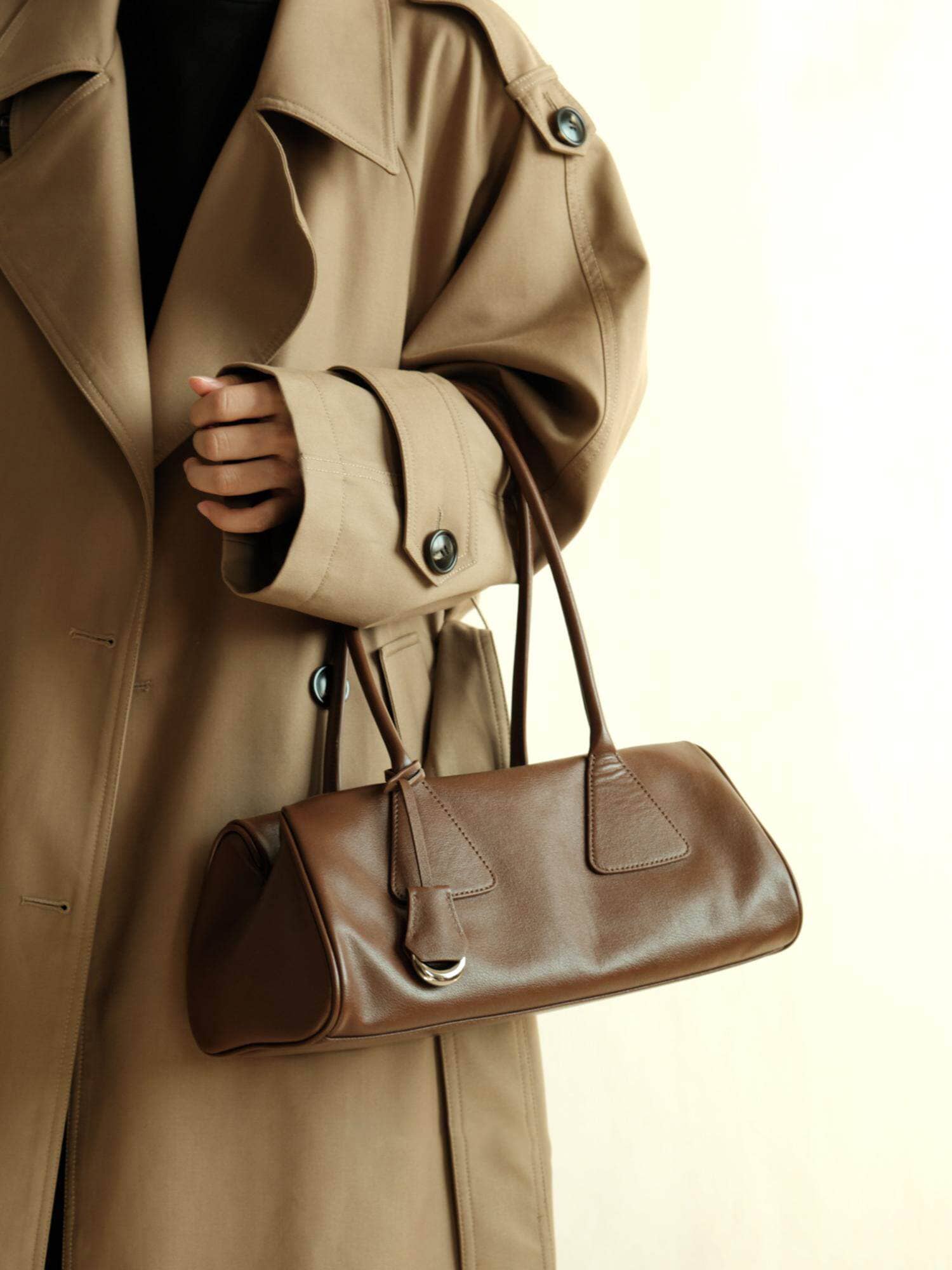 Model wearing a beige trench coat carrying a brown genuine leather shoulder bag