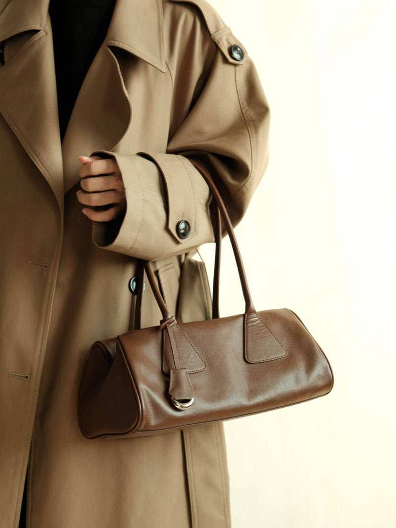 Model wearing a beige trench coat carrying a brown genuine leather shoulder bag