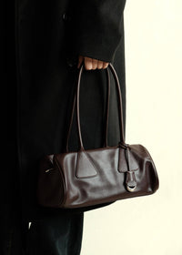 Woman holding a dark burgundy genuine leather handbag wearing a stylish black trench coat