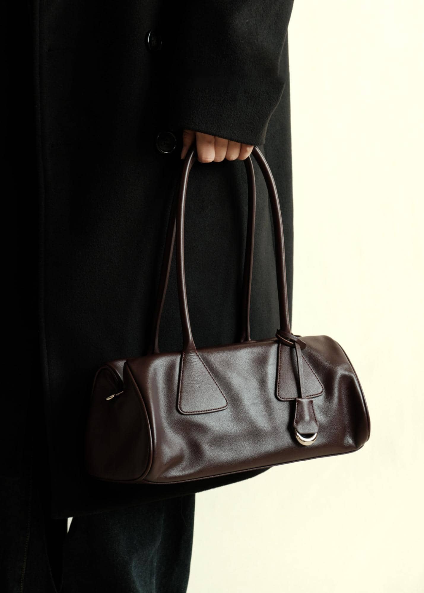 Woman holding a dark burgundy genuine leather handbag wearing a stylish black trench coat