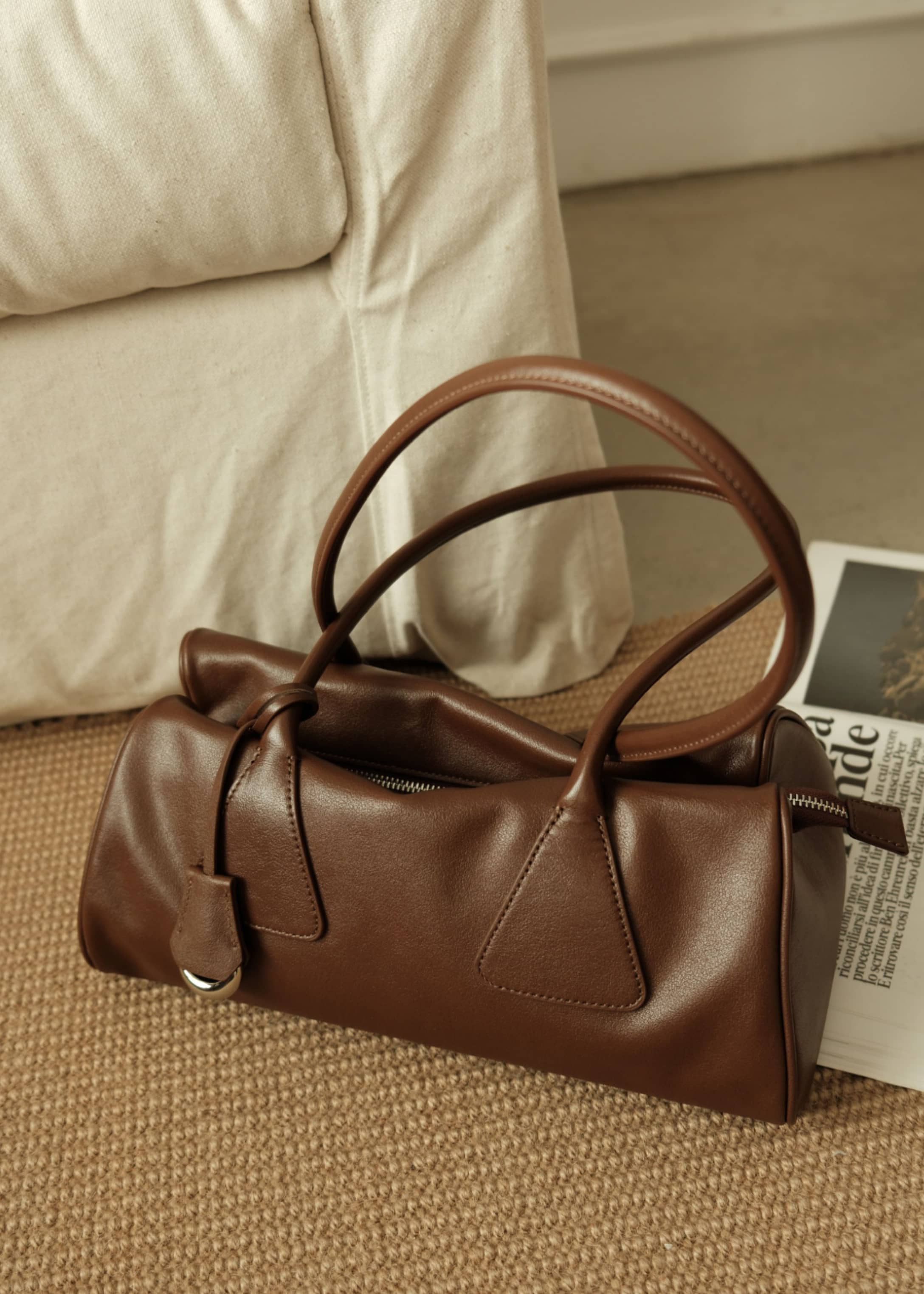 Side view of a brown leather shoulder purse featuring a key tag clochette and silver zipper