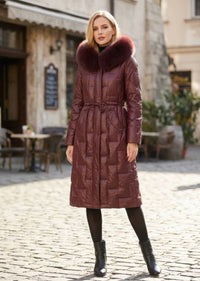 Full length front view of woman wearing burgundy Vivian Seven genuine leather puffer long down parka with fur trim hood