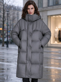 Front view of woman with hands in pockets wearing dark grey high funnel hooded puffer parka