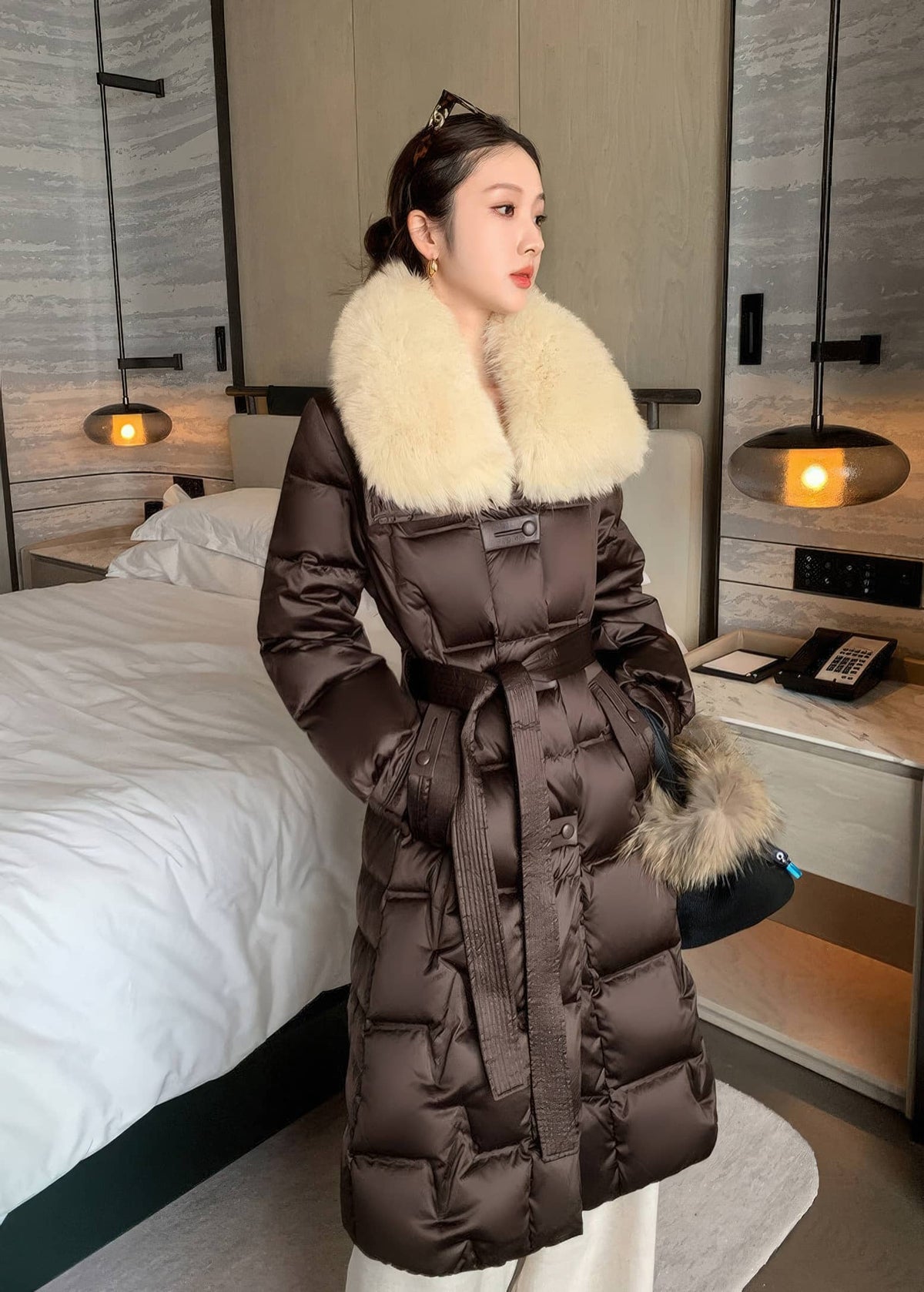 Three-quarter shot of woman in brown long puffer down coat with cream fur collar and tie waist