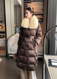 Woman wearing brown long belted puffer down coat with cream fluffy fox fur collar