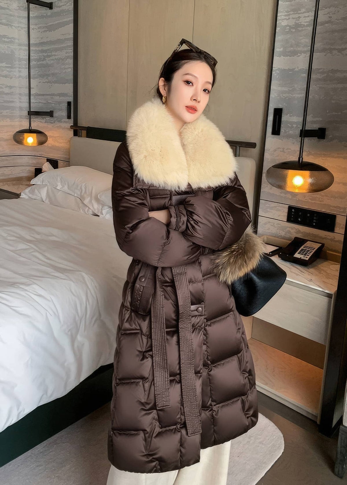 Three-quarter shot of woman with arms crossed wearing brown belted long puffer down coat with cream fox fur collar