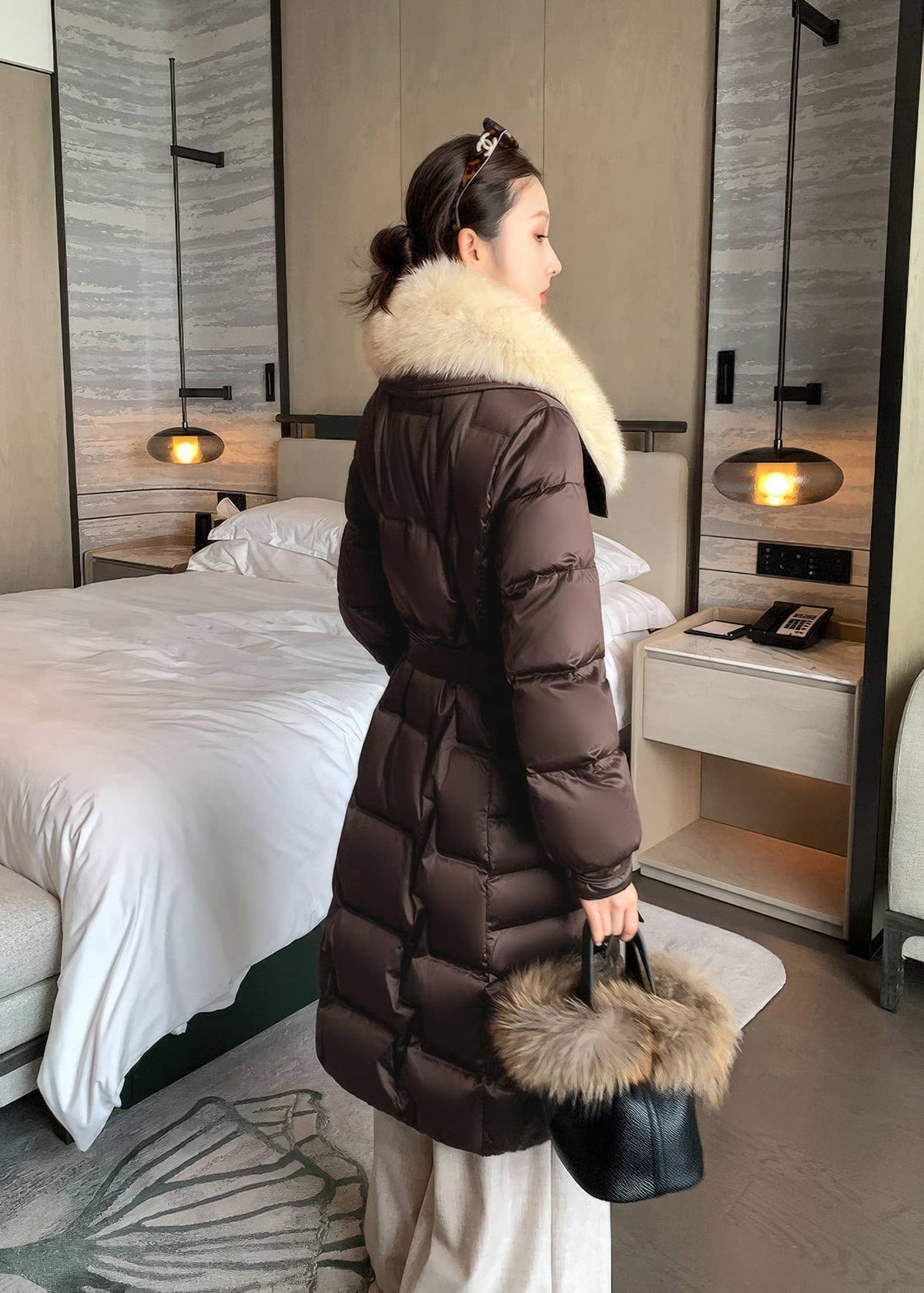Side back view of woman wearing brown quilted long down coat with cream fox fur collar