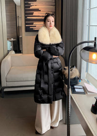 Full length view of woman with arms crossed wearing black long belted puffer coat with cream fox fur collar