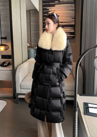 Front view of woman wearing black quilted long down coat with cream fox fur collar and waist belt
