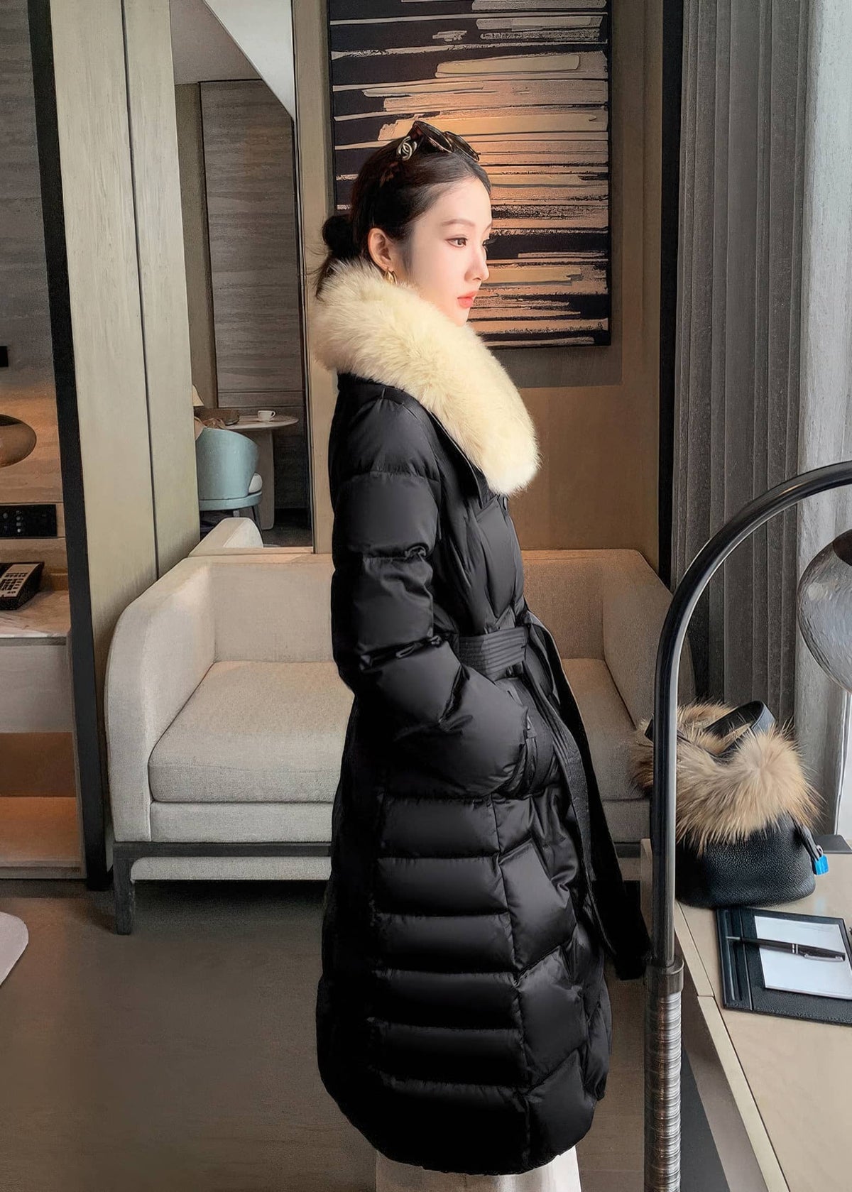 Side view of woman wearing black long puffer down jacket with cream plush fur collar