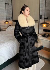 Medium shot of woman wearing black quilted long down coat featuring cream fox fur collar and tied belt
