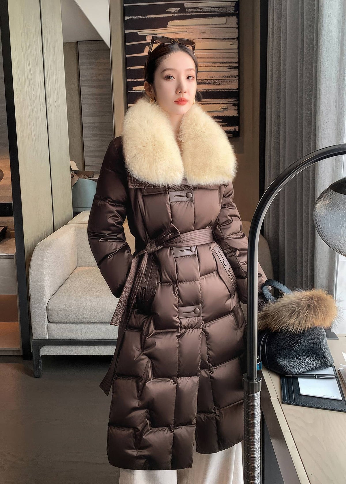 Front portrait view of woman wearing brown long puffer down coat with cream plush collar