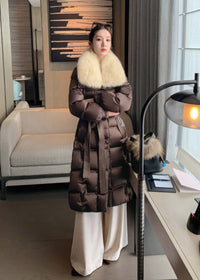 Full length view of woman wearing brown quilted long down coat with cream fox fur collar and cream trousers