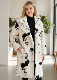 Three-quarter front view of a blonde woman wearing a black and white cow print faux shearling coat with hand in pocket. 