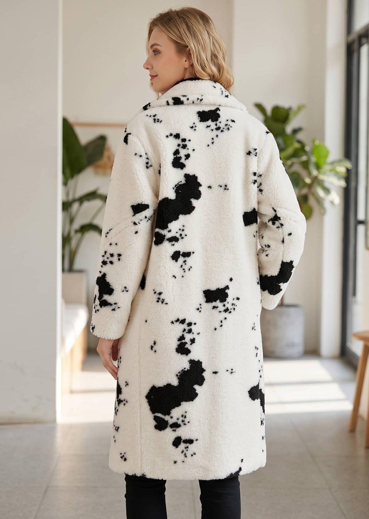 Full-length back view showing the relaxed silhouette, knee-length hem, and all-over cow spot pattern of the faux shearling coat. 
