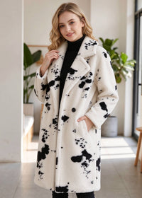 Three-quarter candid indoor portrait of a smiling woman posing in a warm black and white cow print faux shearling midi coat. 