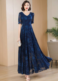 Front view of a woman posing in a navy blue floral burnout maxi dress with a V-neckline and short sleeves, holding a silver clutch while wearing white heeled sandals.