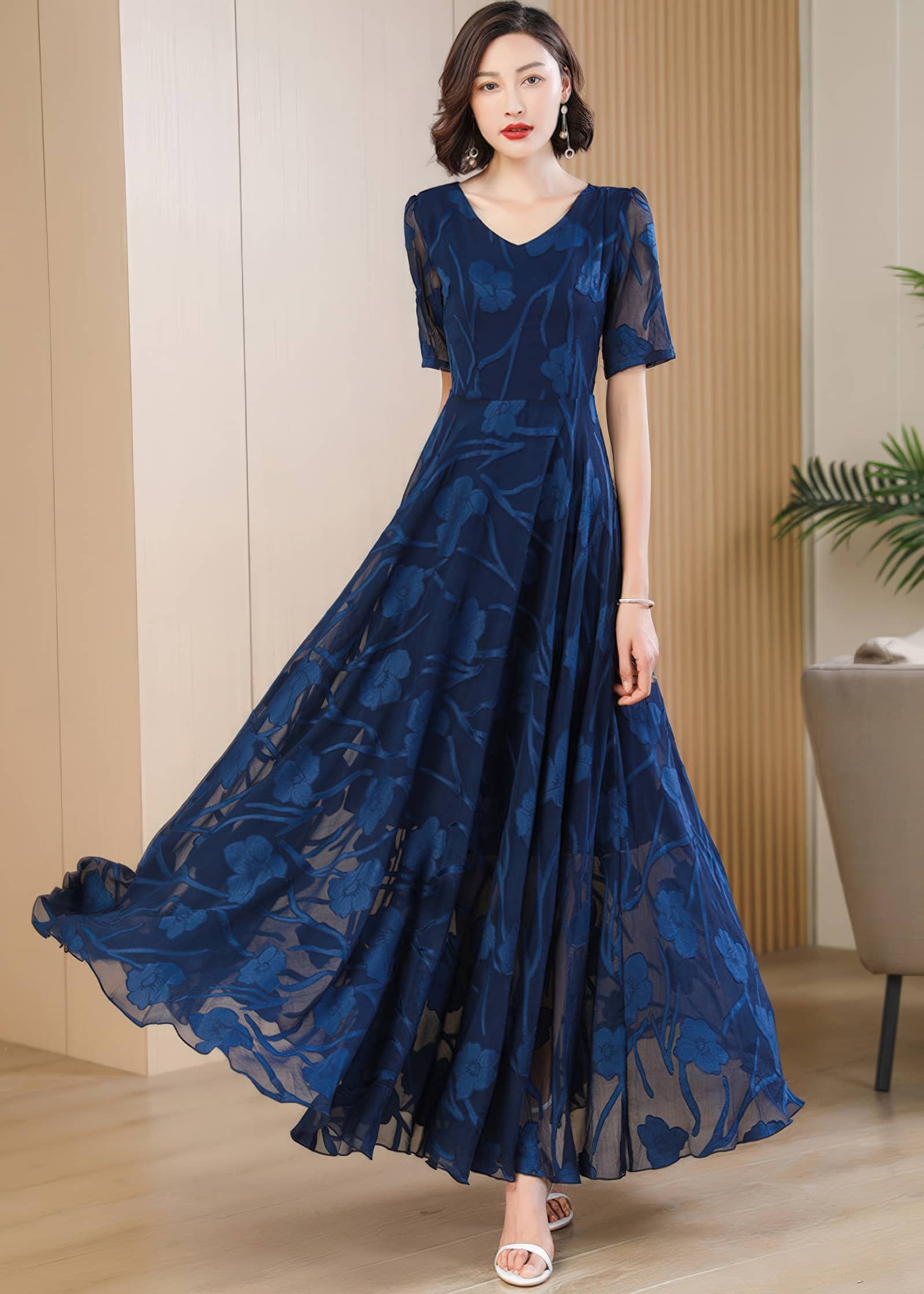 Full-length front view of a woman walking forward in a navy blue floral burnout maxi dress, with the lightweight fabric of the skirt billowing out.