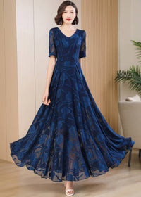 A woman holding out the wide, voluminous skirt of a navy blue floral burnout maxi dress to display its flowy fabric and sheer floral pattern.