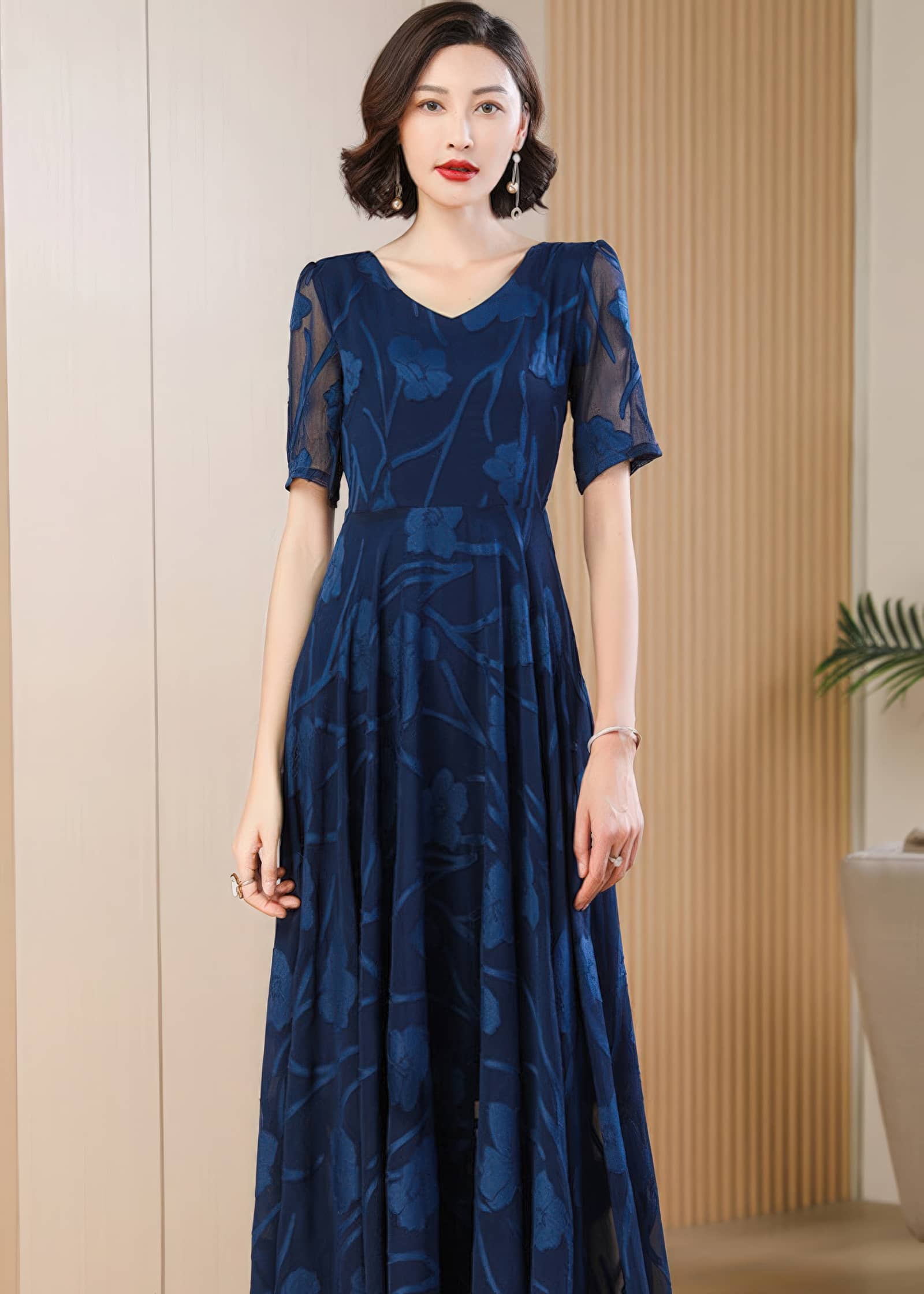 Close-up front view from the waist up of a woman wearing a navy blue V-neck maxi dress with a sheer floral burnout texture and short sleeves.