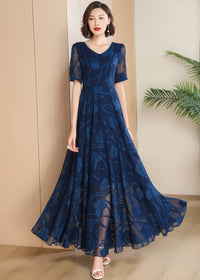Full-length studio portrait of a woman standing and posing in a navy blue floral burnout maxi dress with a flared skirt and white strappy heels.